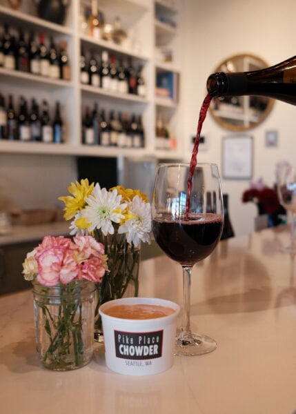 Elegant red wine being poured into a glass with fresh flowers and chowder at Pike Place Chowder, Sea.