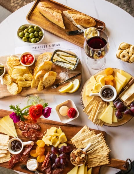 Cheese and charcuterie platter with wine, bread, grapes, and olives for wine pairing.
